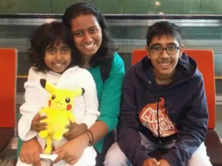 A family of three sitting on a bench with a stuffed toy animal.